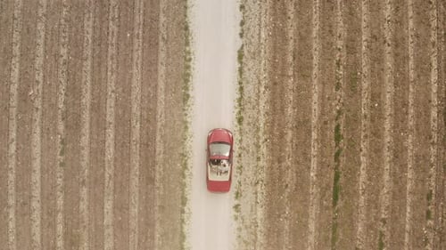 Red Convertible Car Driving on a Country Road Between Plowed Fields