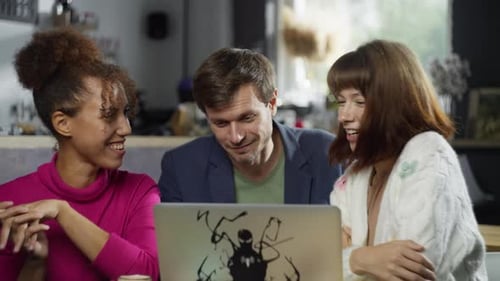 Multiracial Friends Sitting at a Computer in a Cafe and Smiling