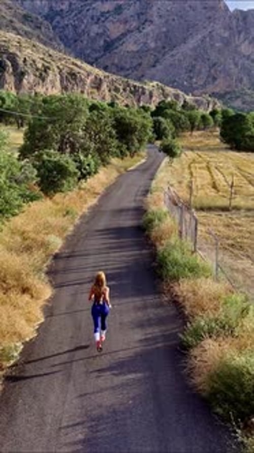 Woman Running on Rural Road Under Mountains