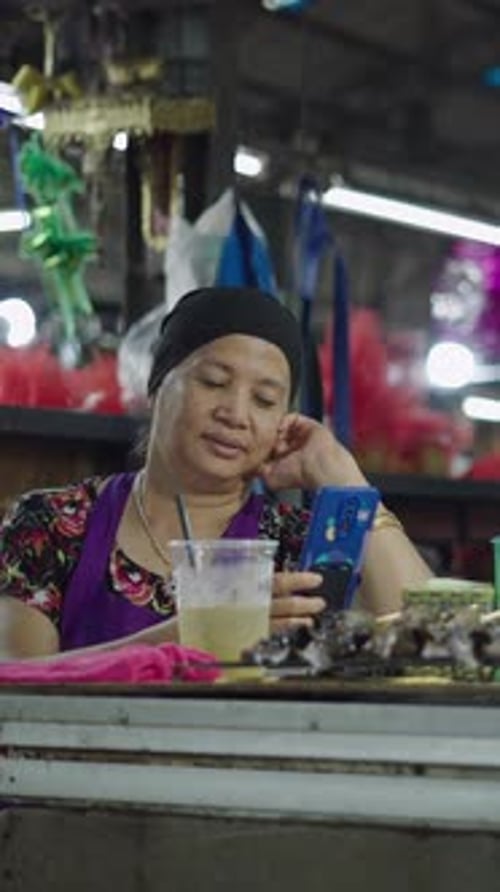 Senhora asiática madura verifica a tela do smartphone dela sentada em sua peixaria