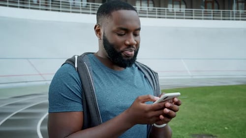 Smiling man using smartphone at outdoor sports track
