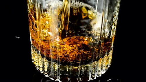 Whiskey is poured into a glass. Slow motion.