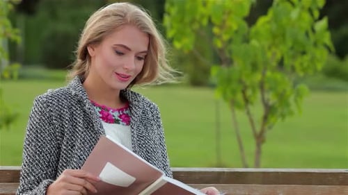 Young Woman Immersed in Reading on a Sunny Park Bench