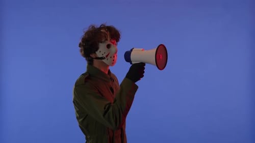 Man in White Mask with Loudspeaker in Hands on Blue Background with Red Neon Light Image of Maniac