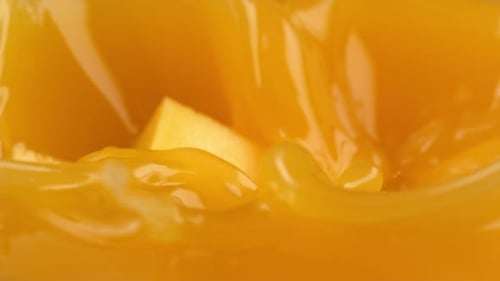 Mango cubes splashing into orange juice close-up shot