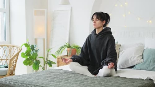 Woman Meditating on Bed in Bright Room