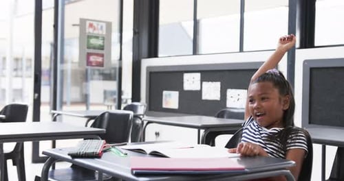 In a school classroom, a young African American girl raises her hand eagerly with copy space