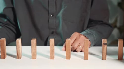 Man hand blocks wood block from many row falling wooden block like domino