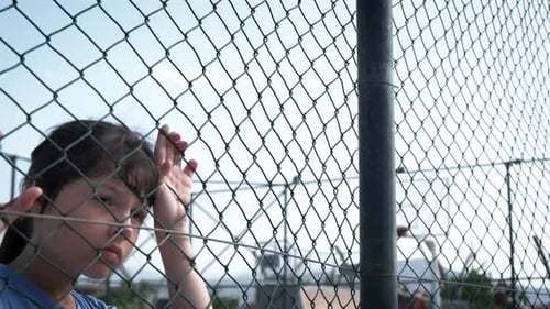 Sad Children Behind a Fence on a Bright Day