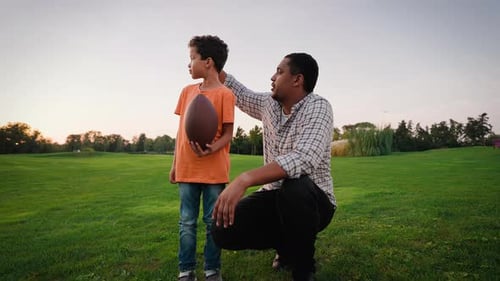 Caring Father Teaching Kid to Play Rugby on Green Meadow