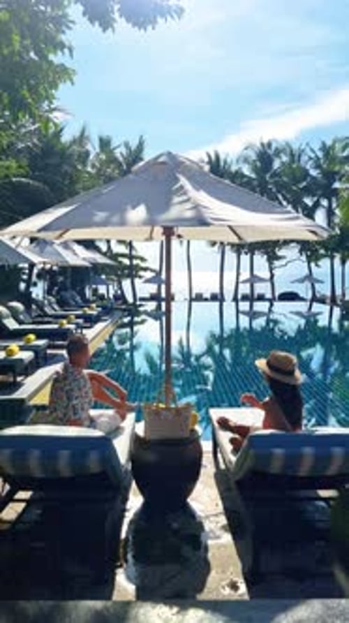 Two People Relax By a Pool Mirrored By the Clear Sky