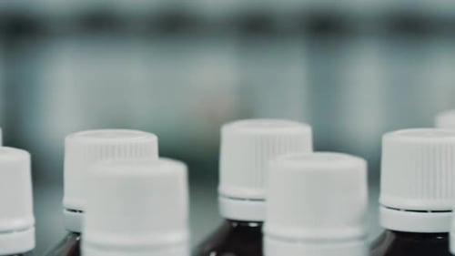 Glass bottles with white plastic caps moves to the packing on the pharmaceutical production line.