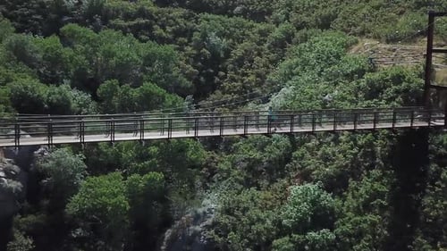 Drone Shot following an active man running on an outdoor hanging suspension bridge above Bear Canyon