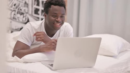 Smiling Man Video Chatting on Laptop in Bed