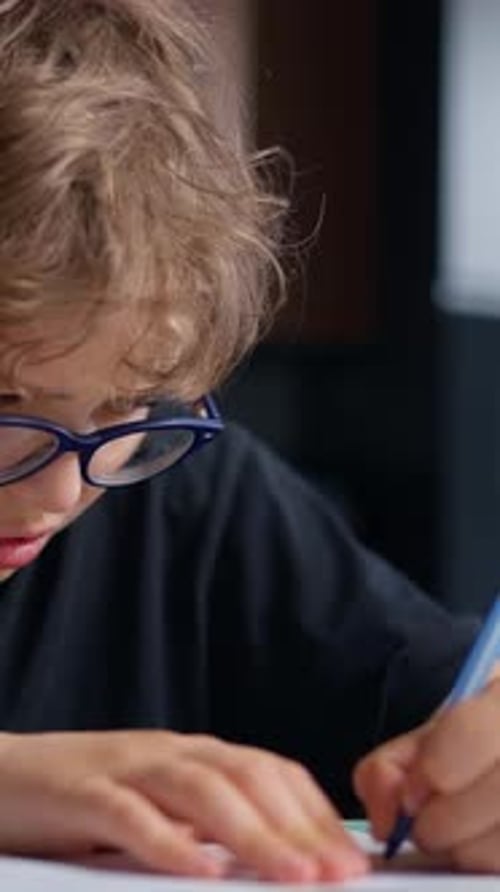 Closeup of a Young Boy Wearing Glasses Focused Intensely on Writing or Drawing with a Pen or Pencil