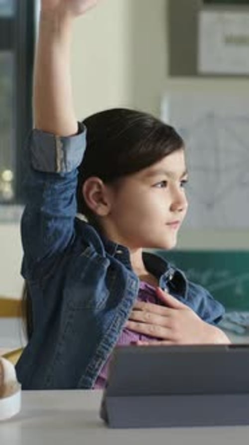 Vertical video: Raising arm after cue student in jean jacket with hand on chest at desk with tablet