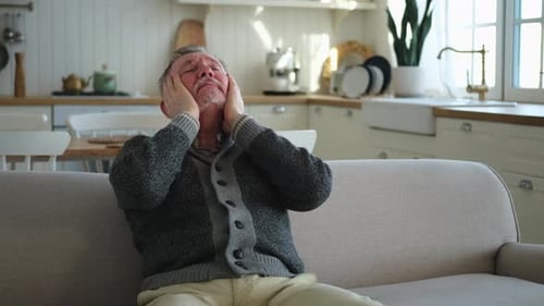 Man Holding Head in Pain on Sofa