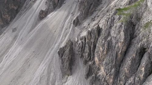 Drone captures Dolomites' steep cliffs and rocky slopes, tilting upwards and moving forward.