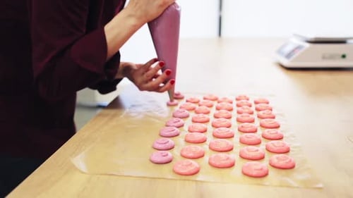 Woman Piping Macarons onto Baking Sheet in Kitchen