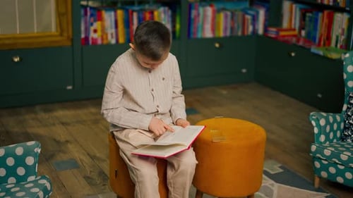 in Bookstore in the Children Area a Handsome Little Boy in Light Clothes Reads a Book