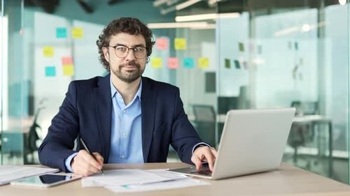 Portrait of a happy financier in a formal suit sitting at a desk at workplace in a business office.