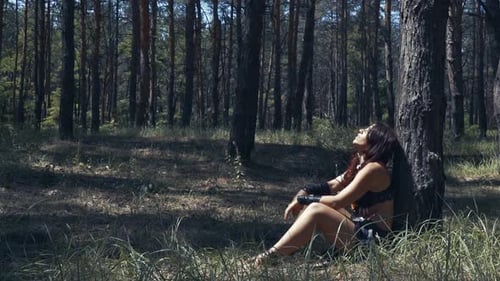 Amazon woman in leather clothes is resting under a tree in the forest