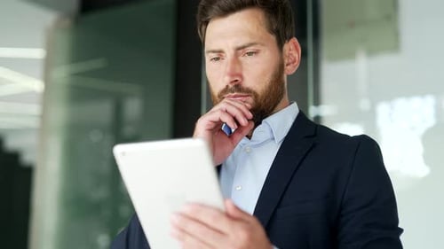 Businessman in formal suit is using digital tablet standing in business office. Worker reads
