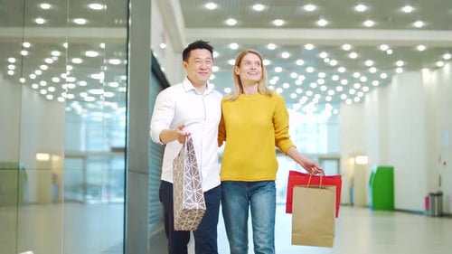 happy multiracial couple asian man and caucasian woman walking together in mall after shopping