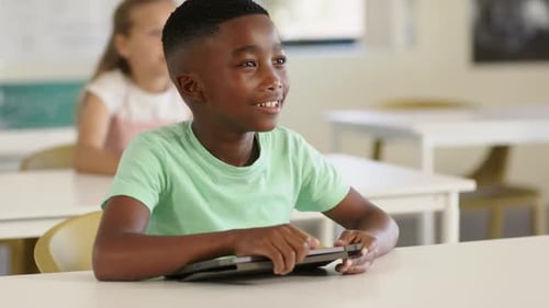 Diverse children learning in class boy with tablet, yellow-shirt boy raising hand after teacher cue