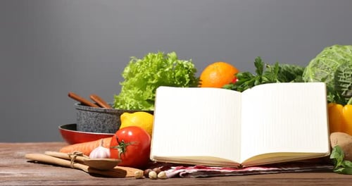 Öffnen Sie das Rezeptbuch und frische Produkte auf einem Holztisch vor grauem Hintergrund. Kamera bewegt sich nach rechts