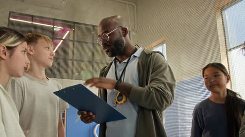 Black Man Giving Instructions to Children in Gym as Coach