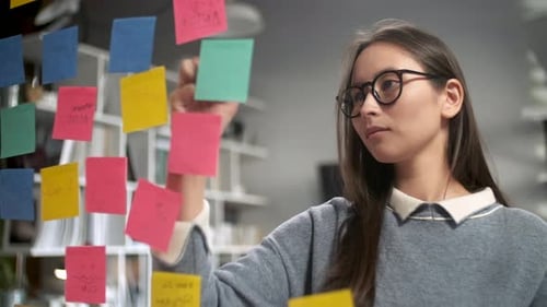 Woman Organizing Colorful Sticky Notes on Glass Wall