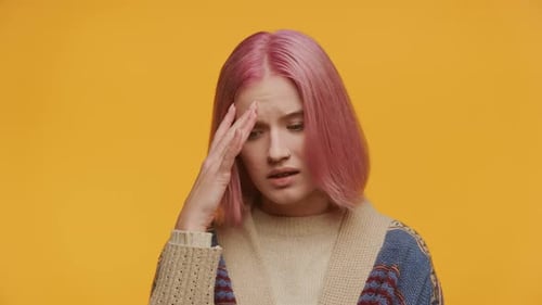 Woman with Pink Hair Rubbing Forehead on Yellow Background
