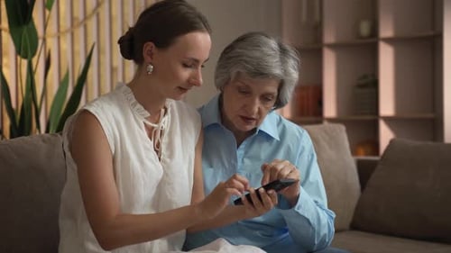 Woman Helping Adult Learn Smartphone Technology Indoors