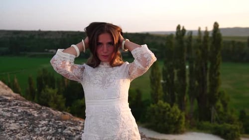 Fröhliche Frau in weißem Boho-Kleid bei Sonnenuntergang in den Bergen Romantische Frau mit langen Haaren stehend mit