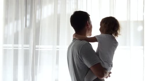 Father Embraces Daughter Holding in Arms While Child Kisses Cheek