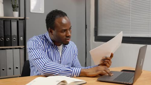 Man Works at Desk with Laptop and Documents