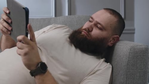 Bearded Man Using Tablet Relaxing on Sofa