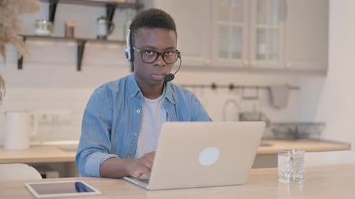 Young African Man with Headset Looking toward Camera in Call Center