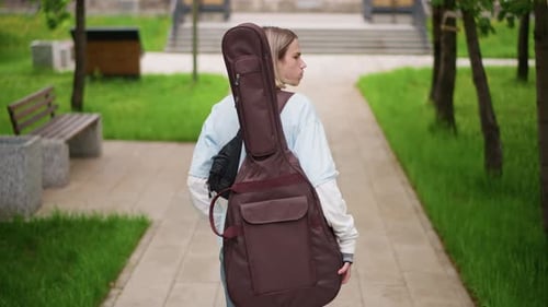 Urban Guitarist Walking Performer Moves Along Treelined Urban Trail Confidently Guitar Player