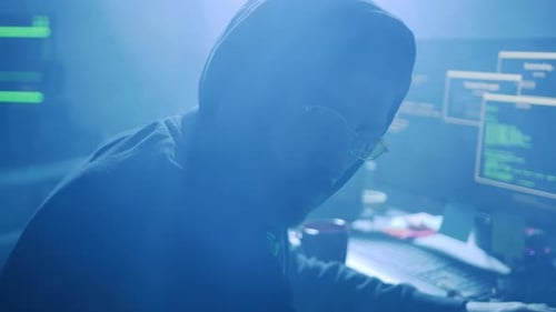 Hooded Figure Coding at Computer in Blue Light