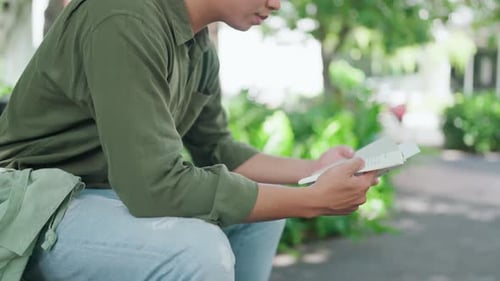 Nahaufnahme eines Mannes, der in einem Park im Freien sitzt und ein Buch liest. Asiatischer Mann trägt ein grünes Hemd