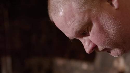 Profile view on face of sweaty caucasian blacksmith forging iron in smithy