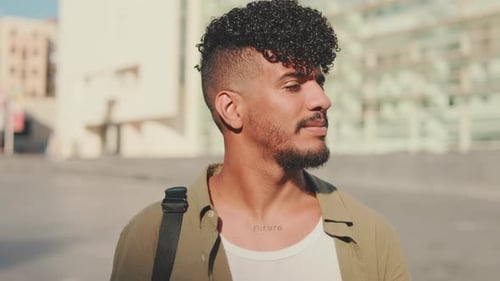 Close up, young student turns his head and smiles at the camera from outside next to the university