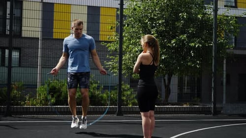 Man Jumping Rope with Woman Watching on Outdoor Court