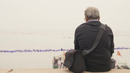 Man with Bag Sits Overlooking River