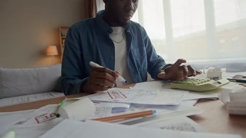 Black Man Using Pen While Reviewing Overdue Bills and Receipts on Table