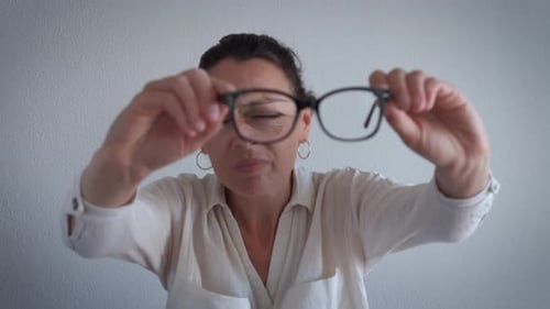 Woman Holds up Pair of Glasses for Inspection