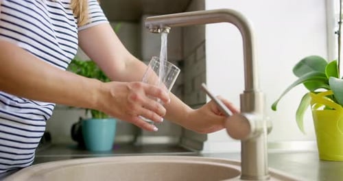Woman Filling Glass with Water at Kitchen Sink