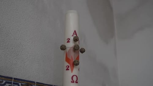 Close-up of a Paschal candle adorned with symbolic elements against a textured wall.